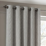 Manhattan silver grey eyelet curtains with textured geometric velvet pattern, hung on a brushed metal rod near a window in a neutral-toned room.