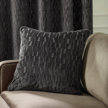 Manhattan Geometric Velvet Cushion in charcoal, square with a cut-velvet raised bar pattern, shown on a beige sofa against a dark curtain backdrop.