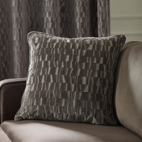 Manhattan Geometric Velvet Cushion in mink with cut-velvet staggered block pattern, shown on a beige sofa against a grey curtain backdrop.