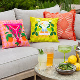Square polyester cushion in lime-green checked print with a margarita cocktail graphic, limes and "Margarita Time" text, styled on a grey outdoor sofa.