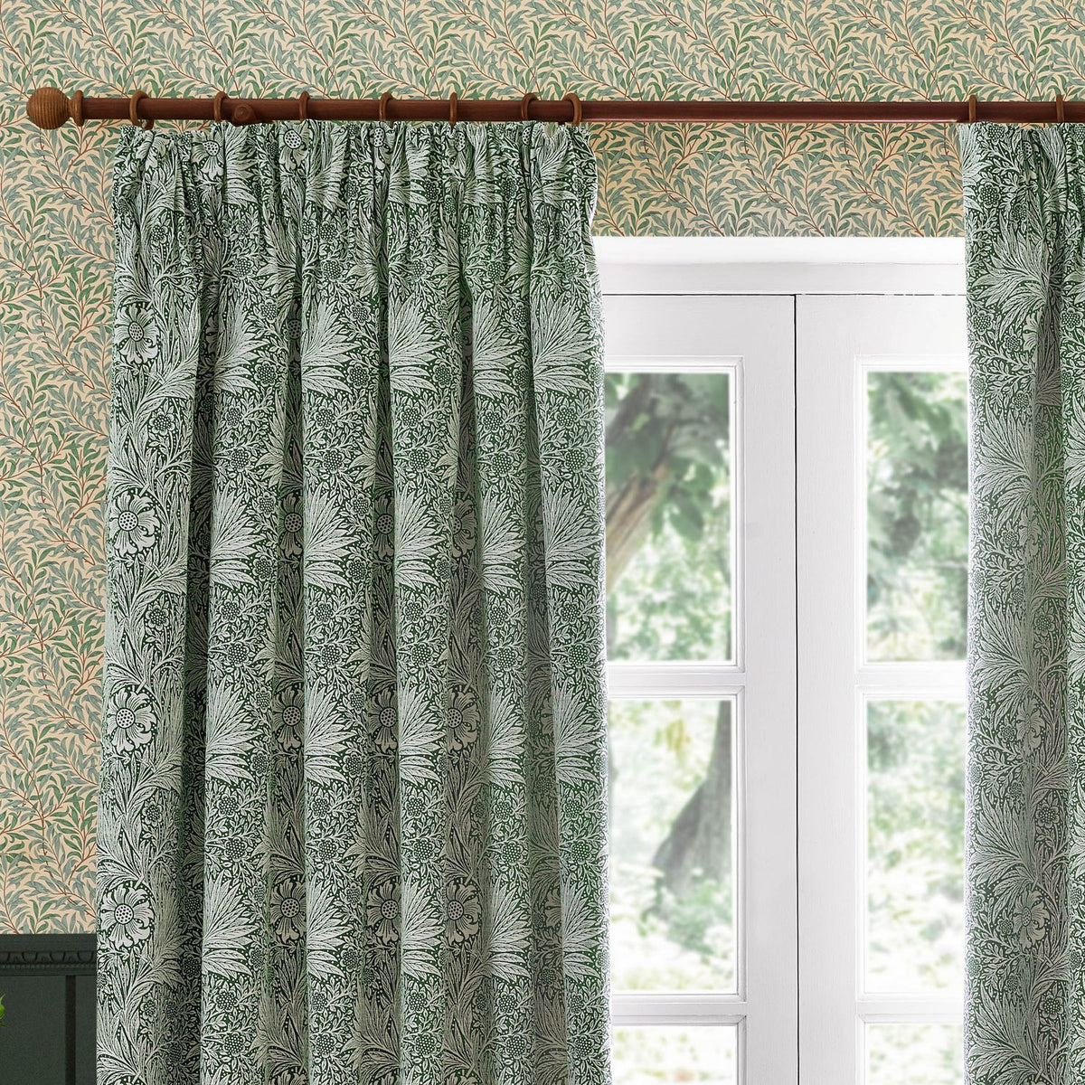 Marigold Jacquard pencil pleat curtains in leaf green, hung on a wooden pole beside a white-framed garden door, showing woven foliage and flower head pattern.