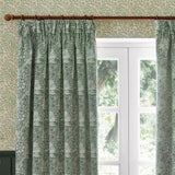Marigold Jacquard pencil pleat curtains in leaf green, hung on a wooden pole beside a white-framed garden door, showing woven foliage and flower head pattern.