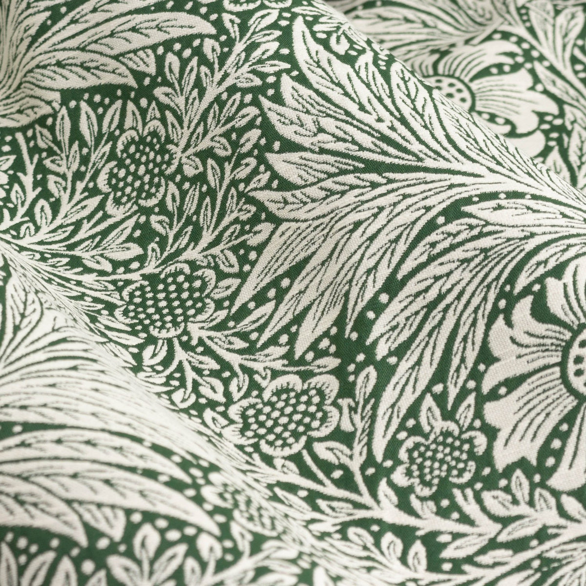 Close-up of Marigold Jacquard pencil pleat curtain fabric in leaf green, showing woven foliage and flower head pattern in deep green on a paler ground.