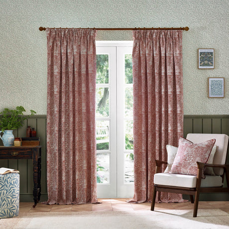 Marigold Jacquard pencil pleat curtains in russet with woven foliage and sunburst pattern, shown pleated on a wooden pole beside French doors in a living room setting.