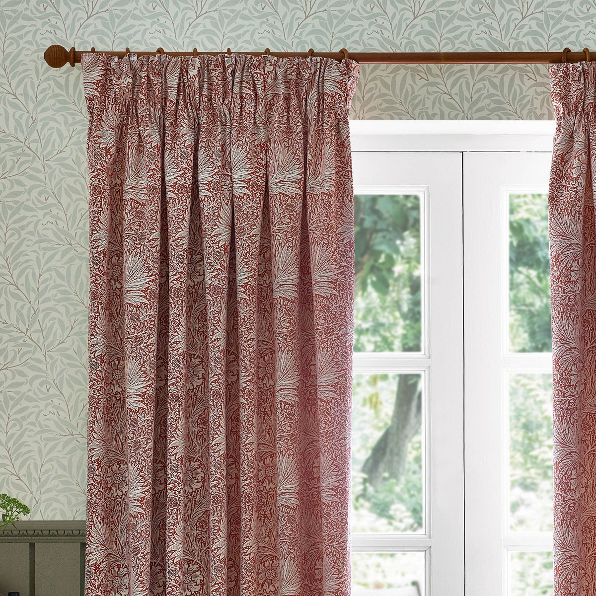 Marigold Jacquard pencil pleat curtains in russet, showing a foliage and sunburst floral pattern woven in polyester, hung on a wooden pole beside a white-framed window.