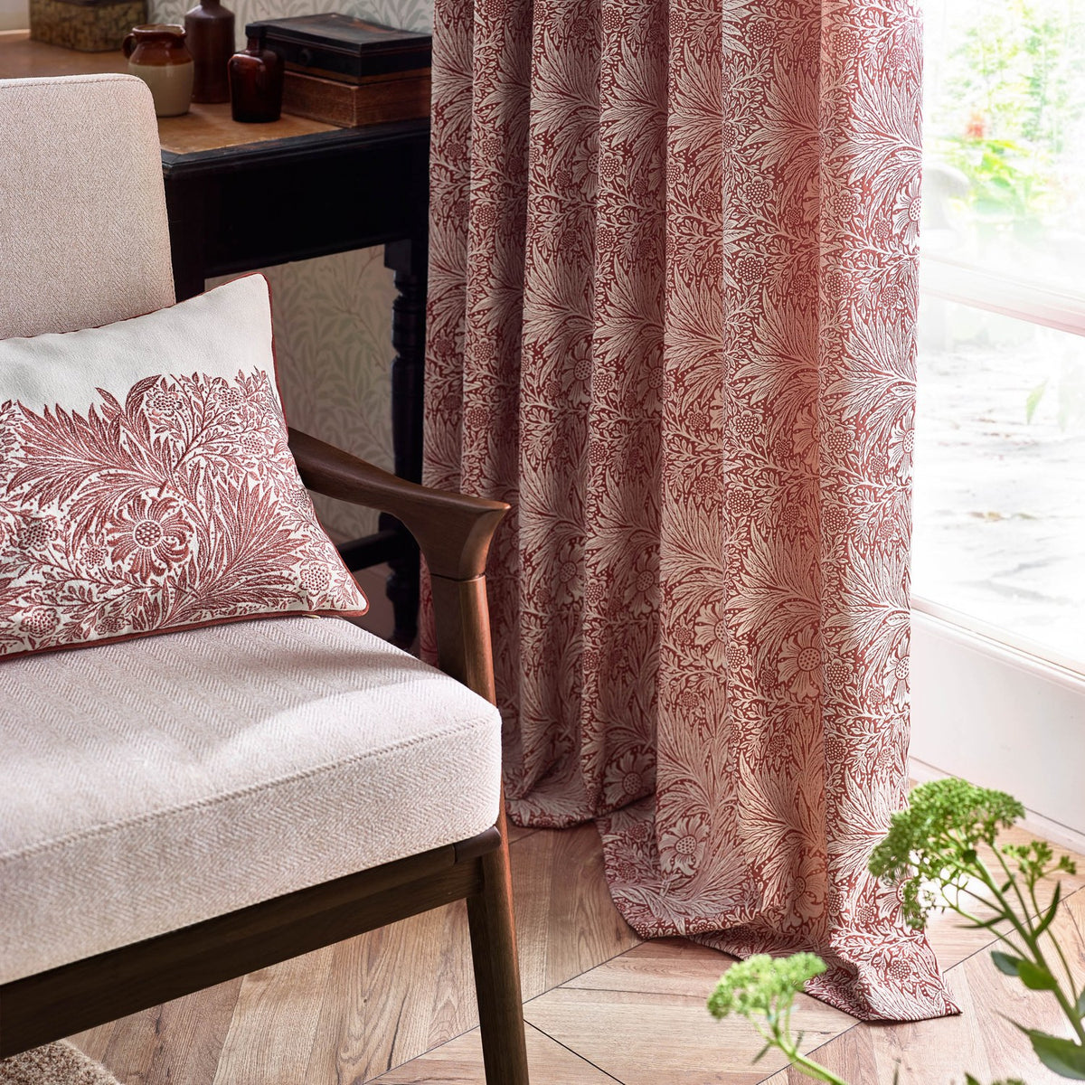 Marigold Jacquard pencil pleat curtains in russet foliage pattern, shown pooling on a wooden floor beside a matching cushion and armchair in a living room setting.