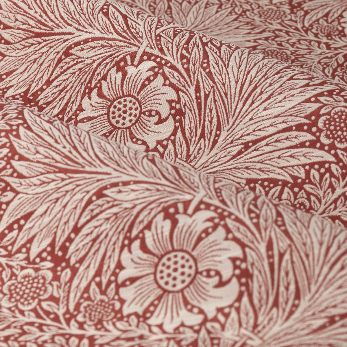 Close-up of Marigold jacquard pencil pleat curtain fabric in russet, showing woven foliage and sunburst floral pattern in polyester with folds highlighting the raised texture.