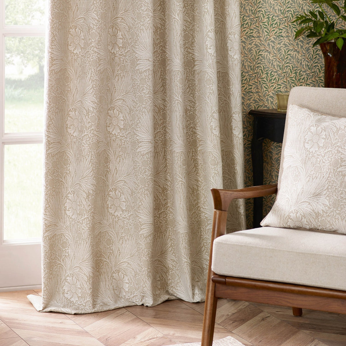 Marigold Jacquard pencil pleat curtains in stone, floral woven pattern, shown pooling on the floor beside a window in a living room with an armchair and matching cushion.