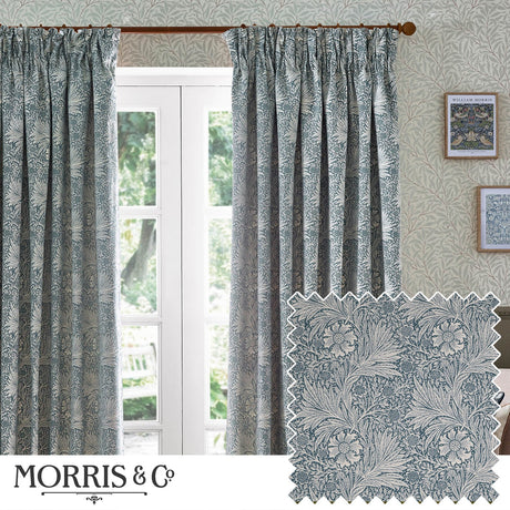 Marigold Jacquard pencil pleat curtains in indigo blue with cream foliage and sunburst pattern, shown pleated at a window in a living room setting.
