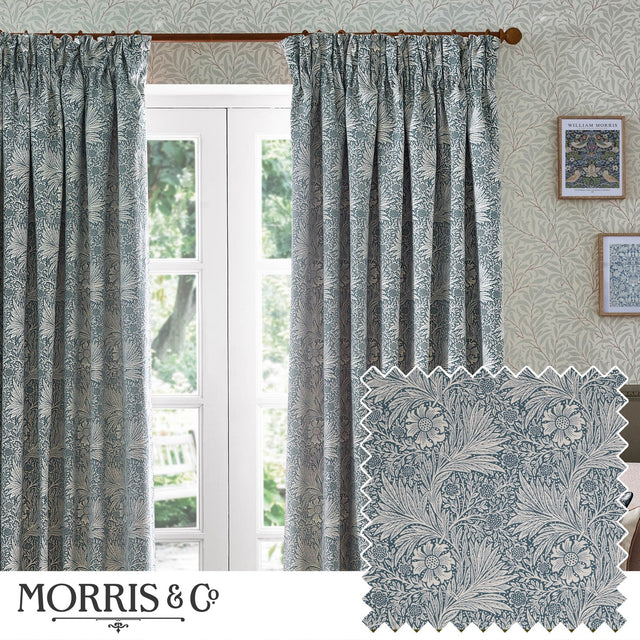 Marigold Jacquard pencil pleat curtains in indigo blue with cream foliage and sunburst pattern, shown pleated at a window in a living room setting.