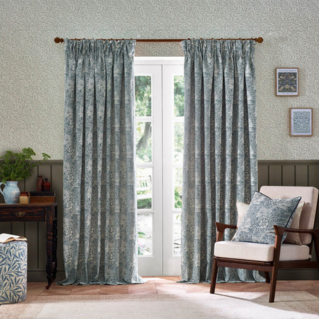 Marigold Jacquard pencil pleat curtains in indigo blue floral pattern on cream fabric, hung by a glazed door in a living room with a matching cushion on an armchair.