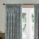 Marigold Jacquard pencil pleat curtains in indigo blue and cream, hung beside a white French door with foliage-patterned wallpaper in the background.