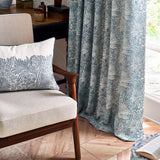 Marigold Jacquard pencil pleat curtains in indigo blue with cream foliage and sunburst pattern, shown pooling by a bright window in a living room setting.