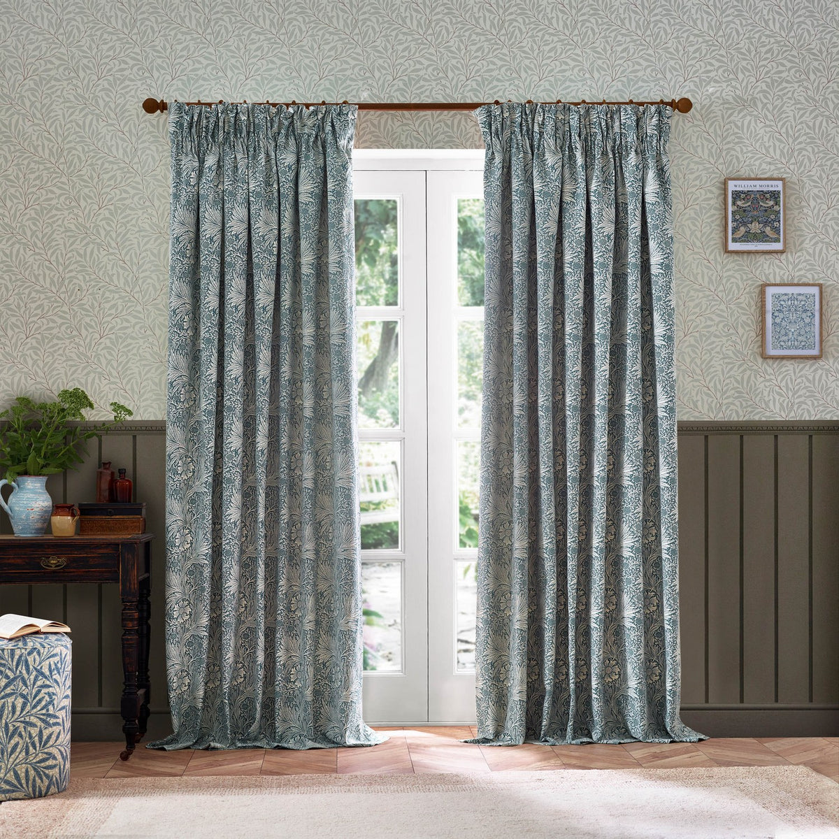 Marigold Jacquard pencil pleat curtains in indigo blue floral pattern on cream ground, shown pleated at a French door in a living room with patterned wallpaper.