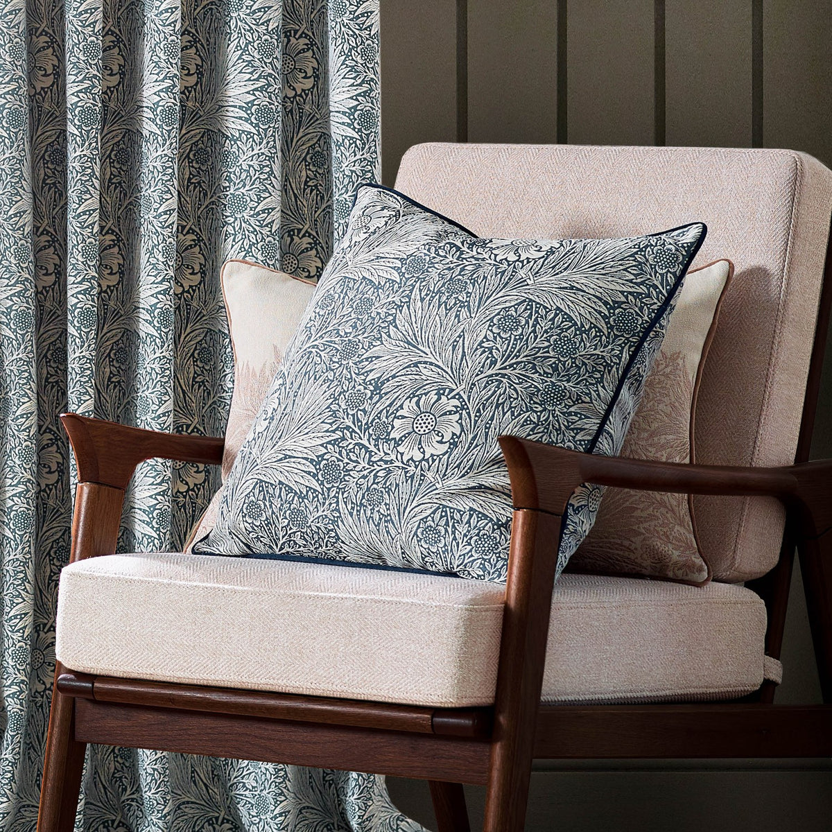 Marigold Jacquard Velvet Cushion in indigo blue with cream floral pattern, shown on a beige armchair with a wooden frame in a living room setting.