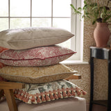 Marigold Jacquard Velvet Cushion in russet red with cream floral pattern, shown as the third cushion in a stacked pile beside a window in a living room setting.