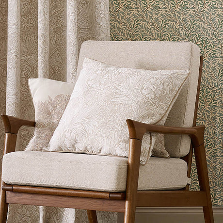 Marigold Jacquard Velvet Cushion in stone, square with woven marigold and foliage pattern, shown on a beige armchair beside a matching floral print cushion.