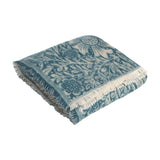 Marigold Jacquard Cotton Throw in indigo, folded showing a woven botanical floral pattern in teal and cream with white fringed edges, on a plain white background.