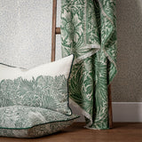Marigold Jacquard Cotton Throw in Leaf Green draped with fringed edges, showing William Morris floral pattern in green on cream, styled with a matching cushion by a wooden ladder.