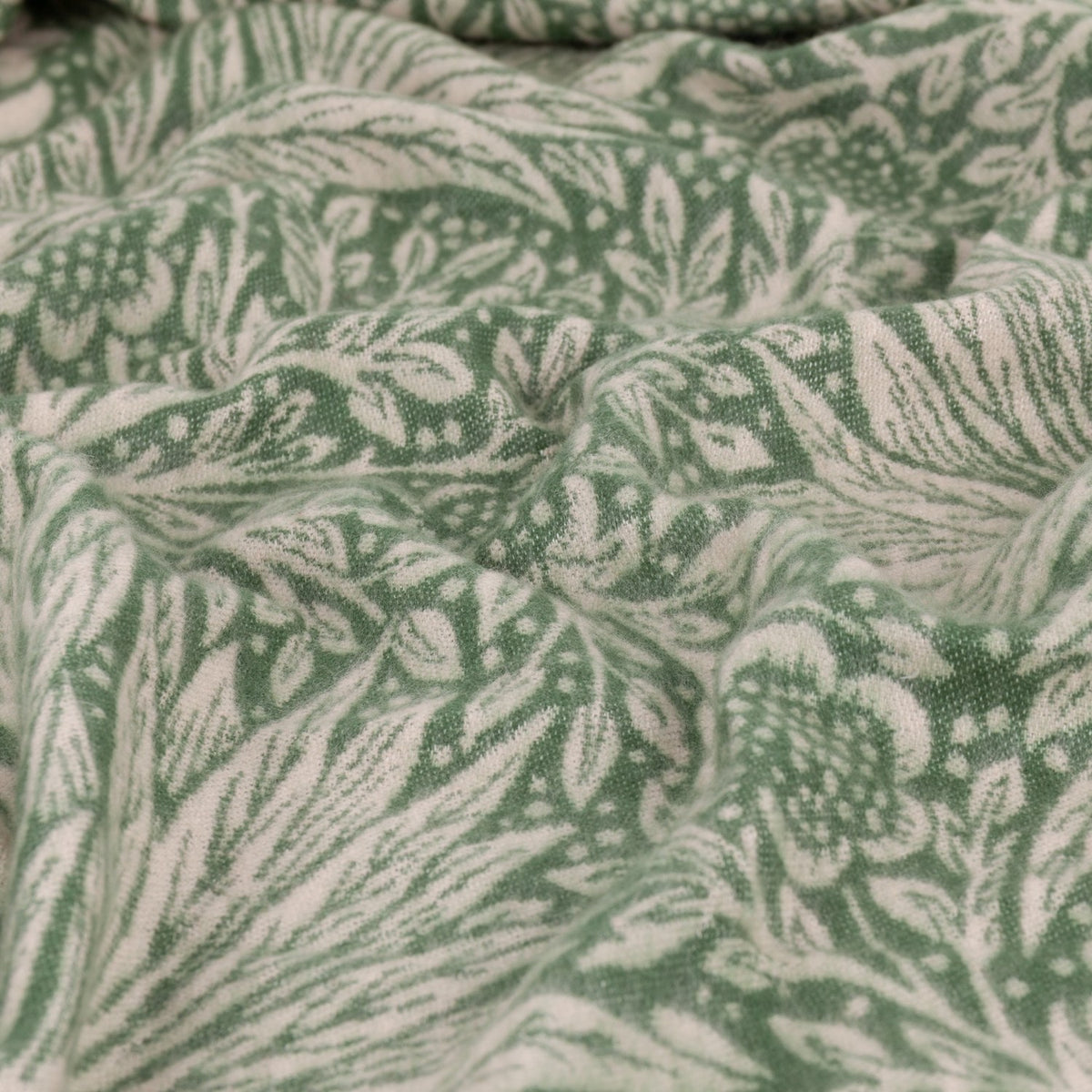 Close-up of the Marigold Jacquard Cotton Throw in Leaf Green, cotton fabric with a woven floral pattern in green and cream, shown draped in folds.