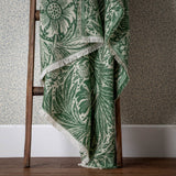 Marigold Jacquard Cotton Throw in leaf green, draped over a wooden ladder with fringed edges, showing William Morris floral pattern on cream ground.