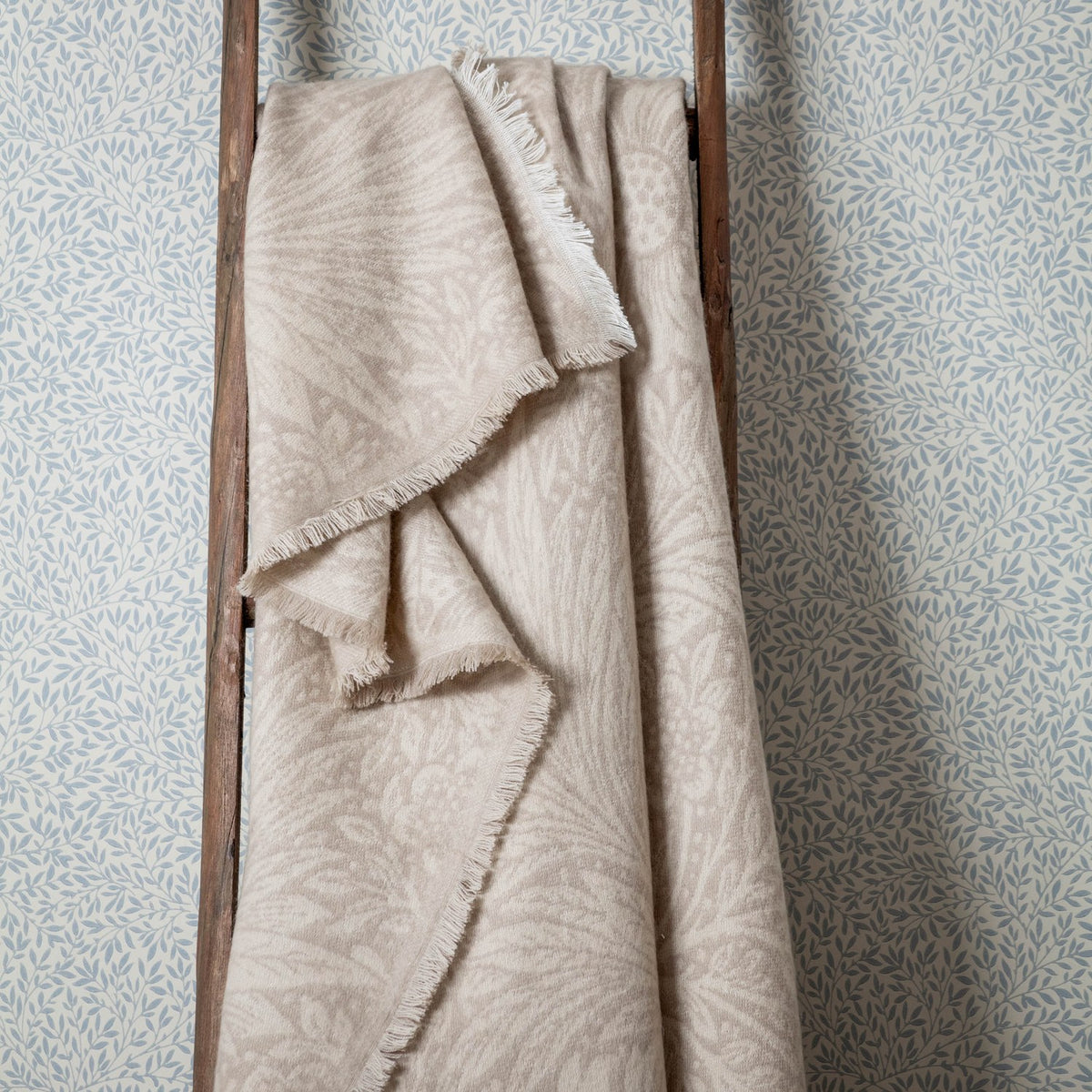 Marigold Jacquard Cotton Throw in stone, draped over a wooden ladder, showing a fringed edge and tonal woven leaf and floral pattern.