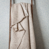 Marigold Jacquard Cotton Throw in stone, draped over a wooden ladder, showing a fringed edge and tonal woven leaf and floral pattern.