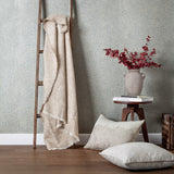Marigold Jacquard Cotton Throw in stone, draped over a wooden ladder, showing a fringed edge and tonal floral jacquard pattern in a living room setting.