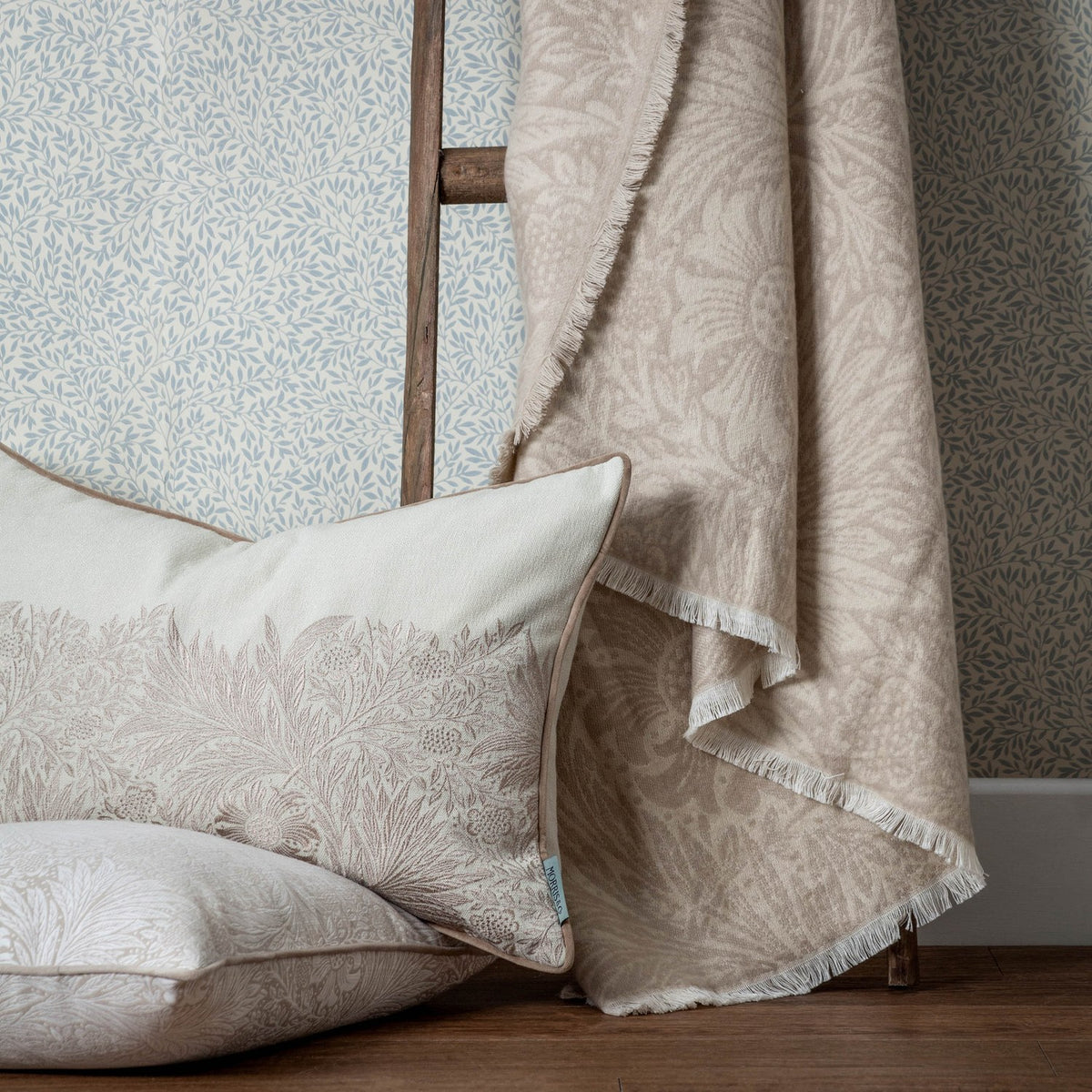 Marigold Jacquard Cotton Throw in stone, draped over a chair beside a matching floral cushion, with fringed edges and a tonal woven leaf and bloom pattern.