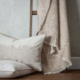 Marigold Jacquard Cotton Throw in stone, draped over a chair beside a matching floral cushion, with fringed edges and a tonal woven leaf and bloom pattern.