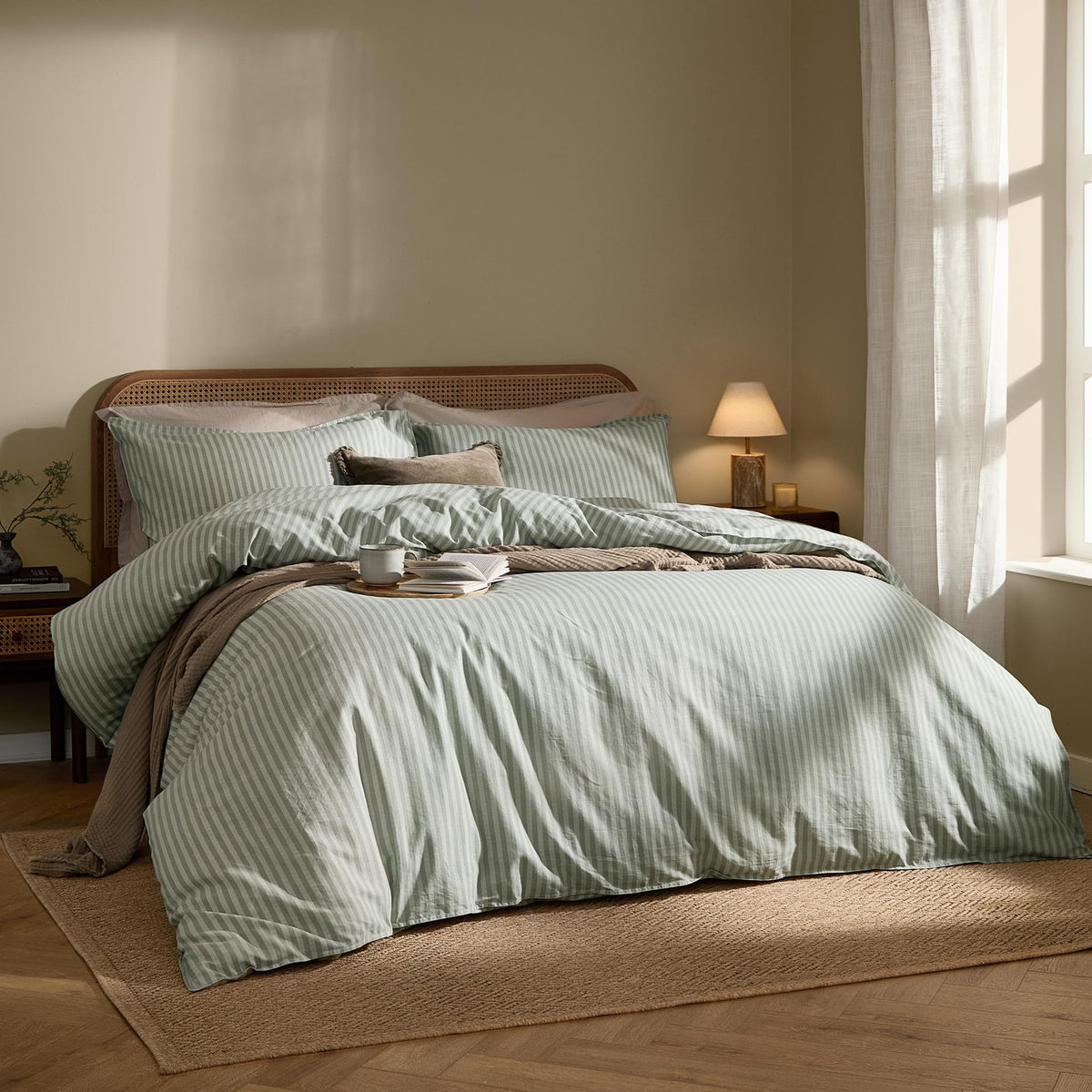 Marlow Stripe Cotton Printed Duvet Cover Set in artichoke/sage on a bed with matching pillowcases, styled in a warm-toned bedroom with rattan headboard and jute rug.