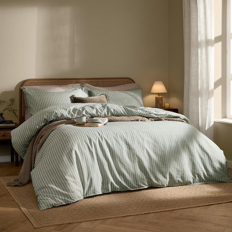 Marlow Stripe Cotton Printed Duvet Cover Set in artichoke/sage on a bed with matching pillowcases, styled in a warm-toned bedroom with rattan headboard and jute rug.