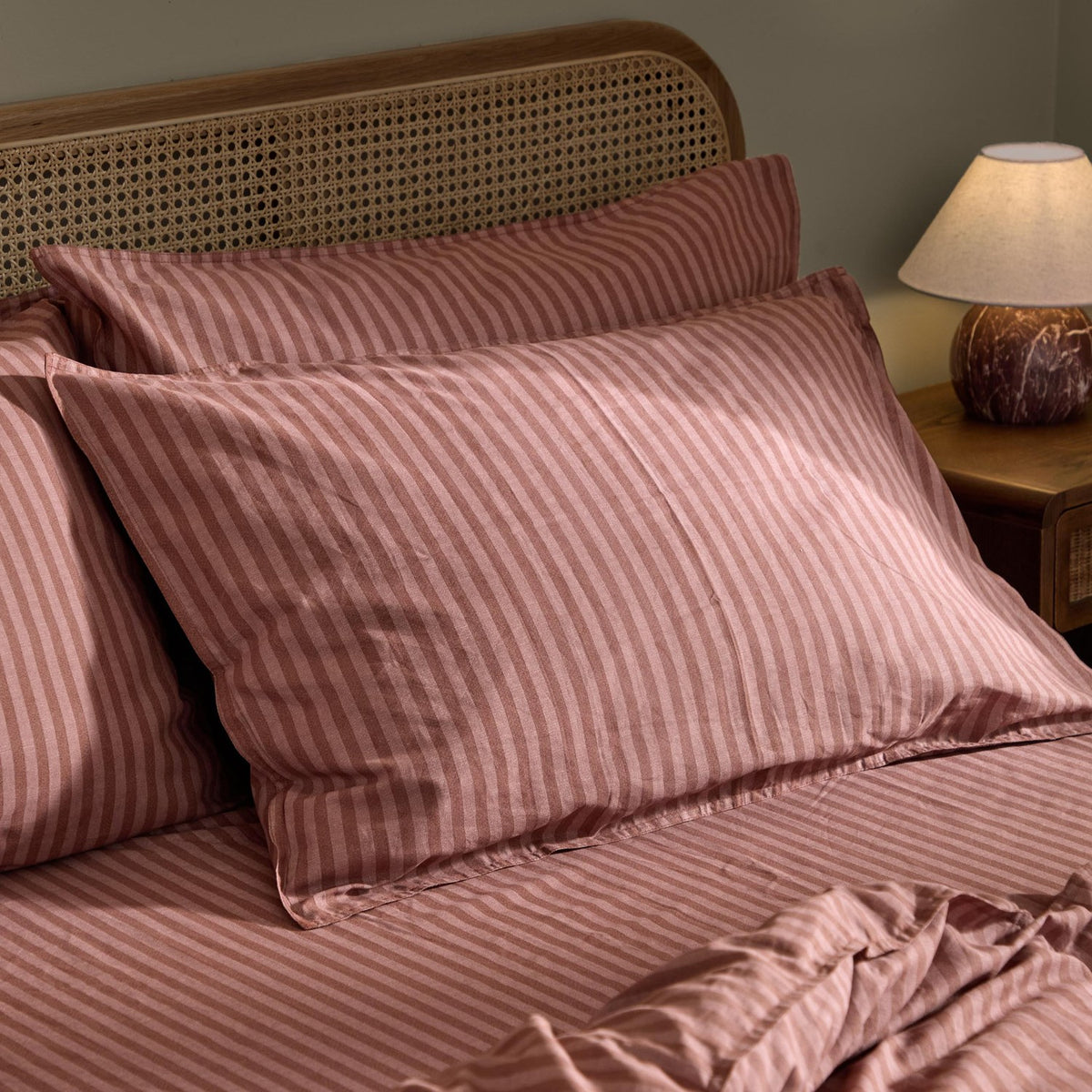 Marlow Stripe Cotton Duvet Cover Set in rosewood pink and chocolate brown, styled with matching pillowcases on a bed with a rattan headboard.