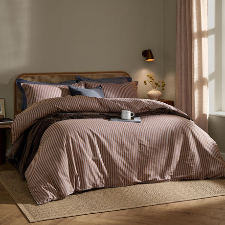 Marlow Stripe Cotton Printed Duvet Cover Set in cocoa/vintage blue on a bed with rattan headboard, styled with navy pillowcases in a bedroom setting.