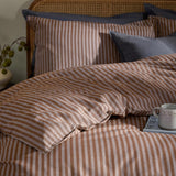 Marlow Stripe Cotton Printed Duvet Cover Set in cocoa brown on a bed with matching pillowcases, styled with vintage blue cushions on a rattan headboard.