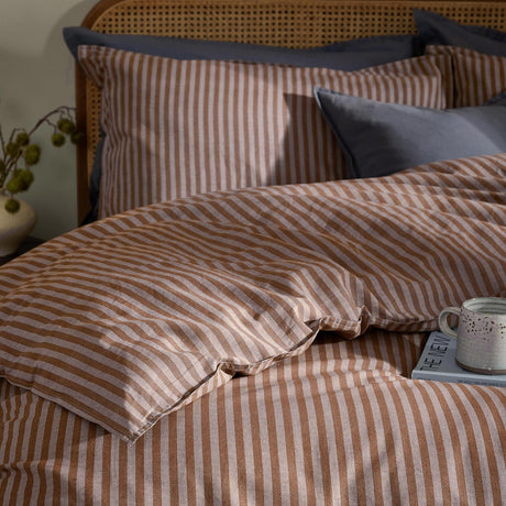 Marlow Stripe Cotton Printed Duvet Cover Set in cocoa brown on a bed with matching pillowcases, styled with vintage blue cushions on a rattan headboard.