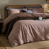 Marlow Stripe Cotton Printed Duvet Cover Set in cocoa brown and vintage blue, styled on a bed with a rattan headboard, layered pillows, and a throw in a bedroom setting.