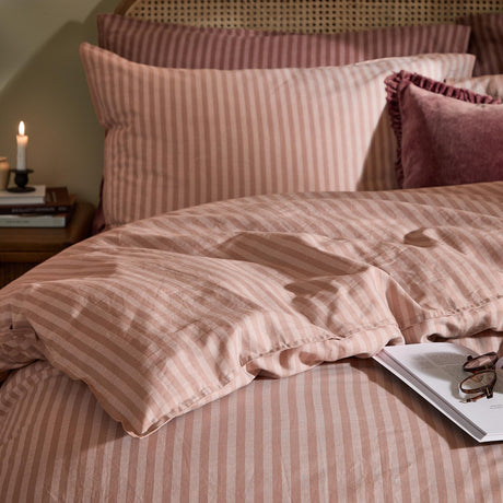 Marlow Stripe Cotton Printed Duvet Cover Set in maple and sandalwood, shown on a bed with matching pillowcases, a velvet cushion, candle, and books on a bedside table.