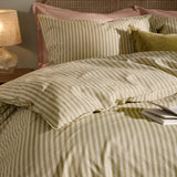 Marlow Stripe Cotton Duvet Cover Set in Oregano/Shell, styled on a bed with matching striped pillowcases, pink pillows, and a green velvet cushion in a bedroom setting.