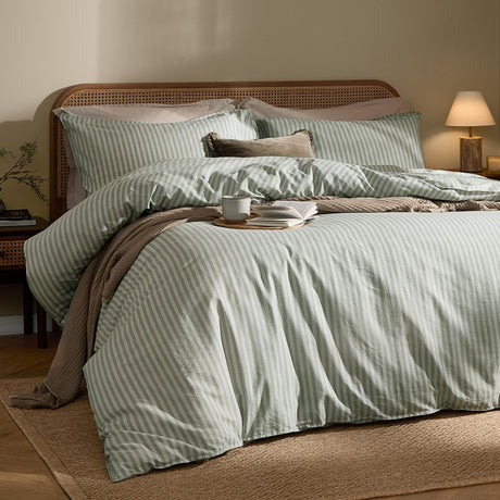 Marlow Stripe cotton pillowcase pair in artichoke/sage on a bed with matching striped duvet cover, styled in a warm-toned bedroom with a cane headboard.