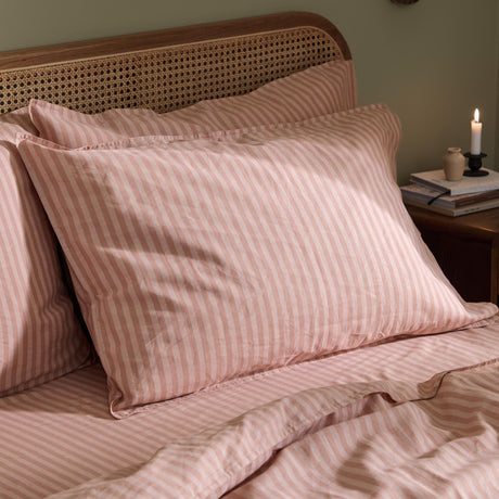 Marlow Stripe Printed Cotton Pillowcase Pair in Maple/Sandalwood, dusky pink and white striped cotton pillowcases styled on a bed with a cane headboard.