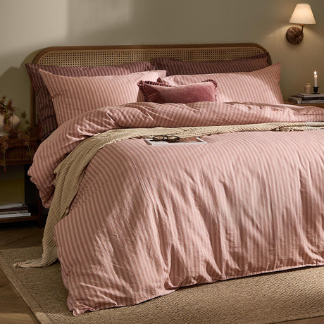 Marlow Stripe Printed Cotton Pillowcase Pair in Maple/Sandalwood shown styled on a bed with matching striped duvet cover, rattan headboard, and a velvet cushion in a bedroom setting.
