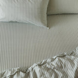 Marlow Stripe Printed Cotton Fitted Sheet in artichoke/sage on a bed, showing fine vertical stripes across the fitted sheet, duvet, and matching pillowcases.