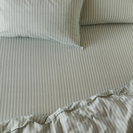 Marlow Stripe Printed Cotton Fitted Sheet in artichoke/sage on a bed, showing fine vertical stripes across the fitted sheet, duvet, and matching pillowcases.