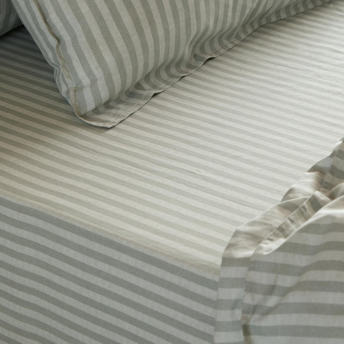 Marlow Stripe Printed Cotton Fitted Sheet in Artichoke/Sage, showing a green and white striped cotton bed sheet with matching pillowcase and elasticated corner detail.