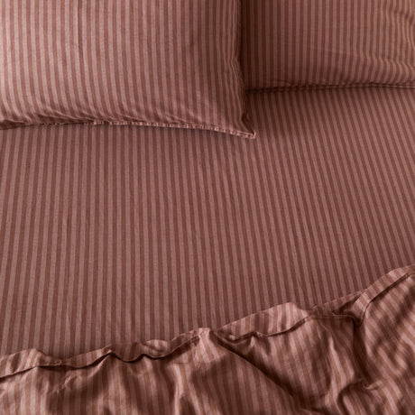 Marlow Stripe Printed Cotton Fitted Sheet in chocolate/rosewood, shown on a bed with matching striped pillowcases, fine tonal stripe pattern and elasticated corners visible.