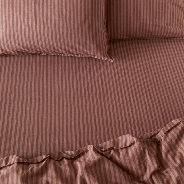 Marlow Stripe Printed Cotton Fitted Sheet in chocolate/rosewood, shown on a bed with matching striped pillowcases, fine tonal stripe pattern and elasticated corners visible.