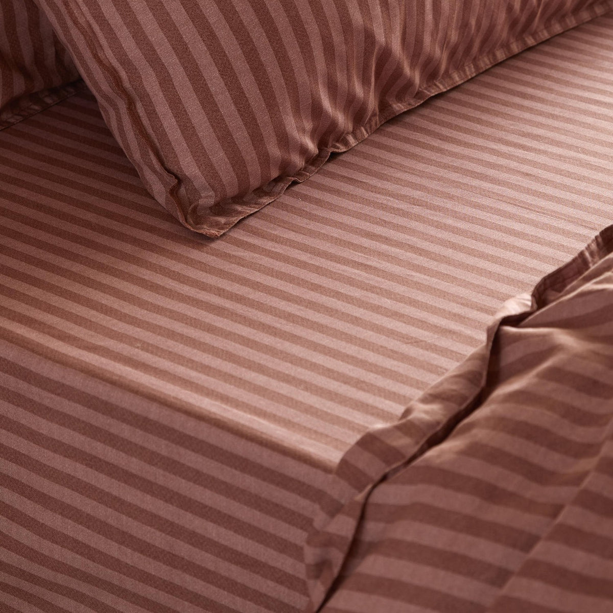 Marlow Stripe Printed Cotton Fitted Sheet in Chocolate/Rosewood, shown fitted to a mattress with matching pillowcase, in a tonal striped cotton finish.