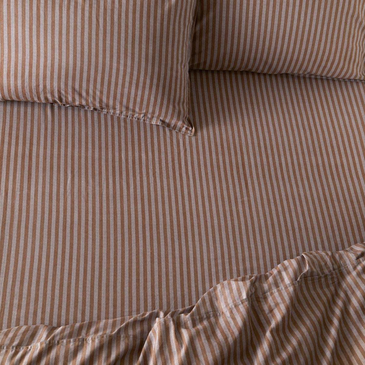 Marlow Stripe Printed Cotton Fitted Sheet in cocoa brown and vintage blue, showing a fine striped pattern on cotton fabric with matching pillowcases on a bed.