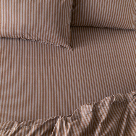 Marlow Stripe Printed Cotton Fitted Sheet in cocoa brown and vintage blue, showing a fine striped pattern on cotton fabric with matching pillowcases on a bed.